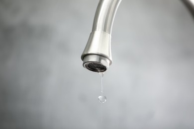 Photo of Save water concept. Water dripping from tap against grey background, closeup