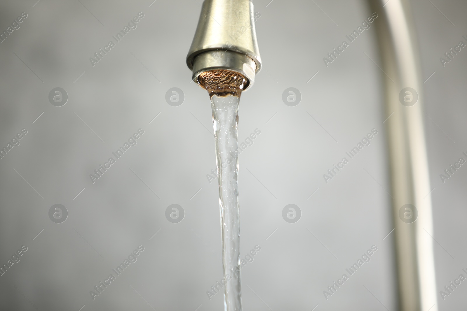 Photo of Save water concept. Stream of water flowing from tap against grey background, closeup