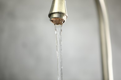 Photo of Save water concept. Stream of water flowing from tap against grey background, closeup