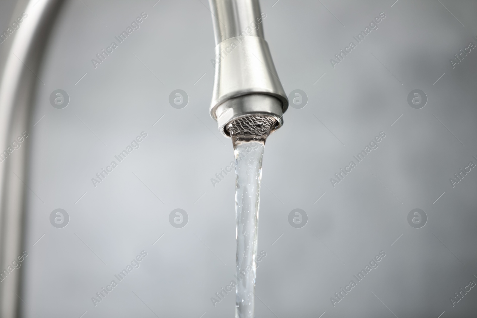 Photo of Save water concept. Stream of water flowing from tap against grey background, closeup