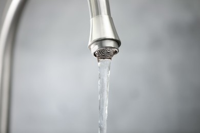 Photo of Save water concept. Stream of water flowing from tap against grey background, closeup