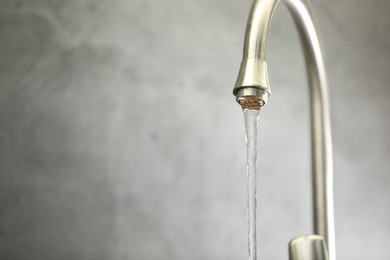 Photo of Save water concept. Stream of water flowing from tap against grey background, closeup. Space for text