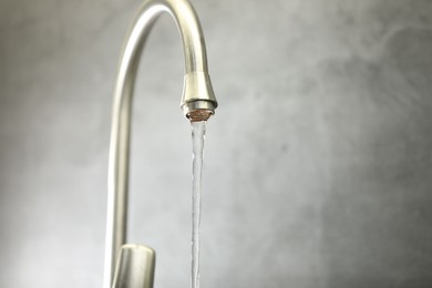 Photo of Save water concept. Stream of water flowing from tap against grey background, closeup. Space for text