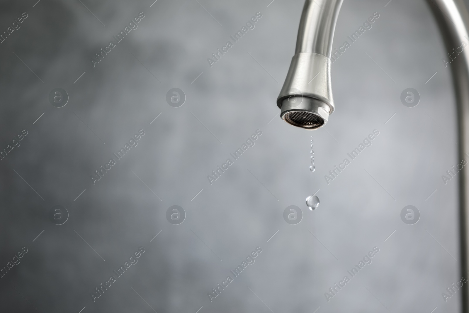 Photo of Water saving concept. Water dripping from tap against grey background, closeup. Space for text