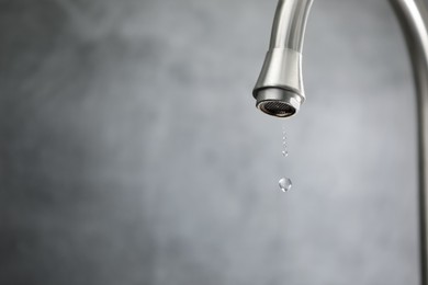Photo of Water saving concept. Water dripping from tap against grey background, closeup. Space for text