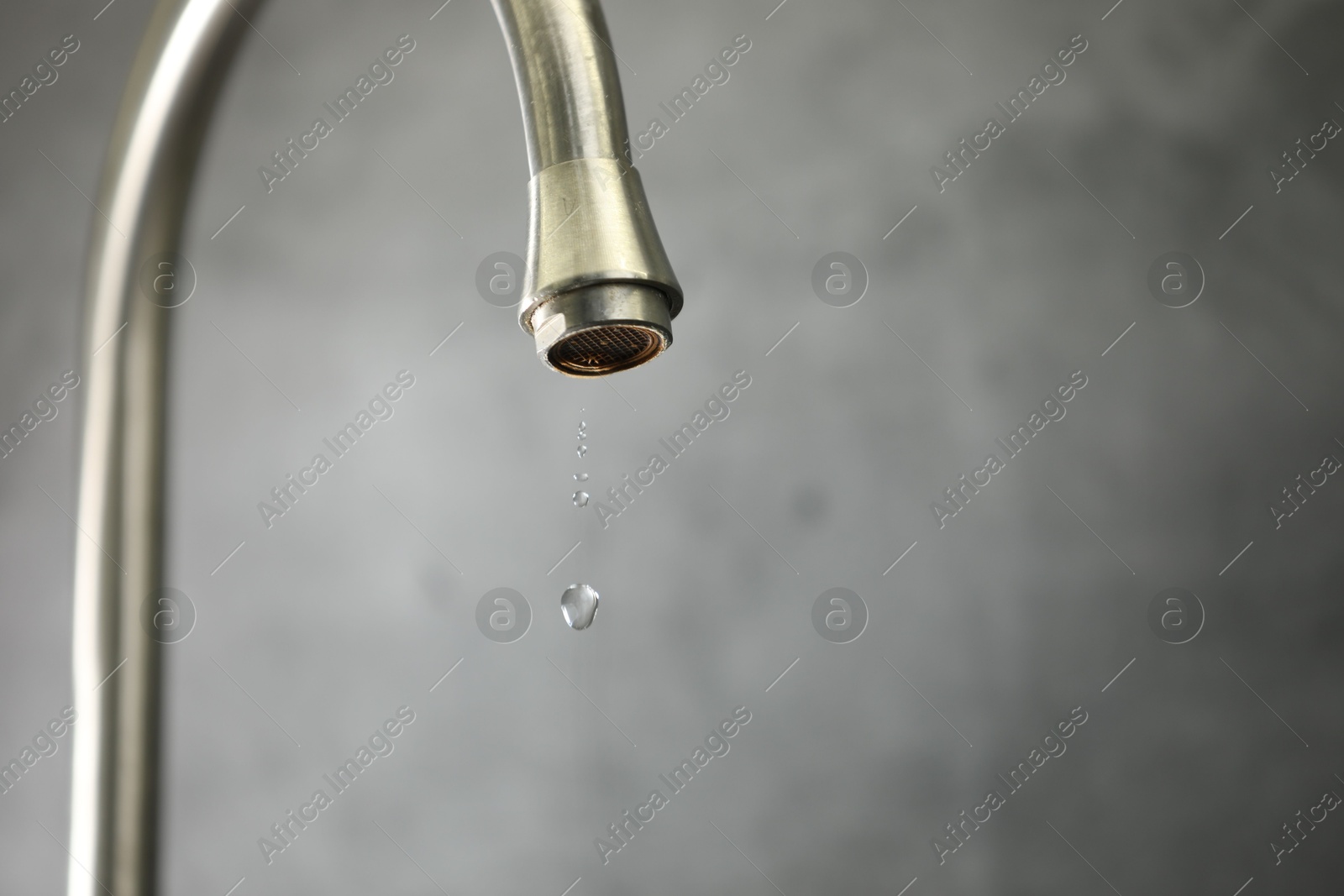Photo of Water saving concept. Water dripping from tap against grey background, closeup. Space for text