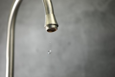 Photo of Water saving concept. Water dripping from tap against grey background, closeup. Space for text