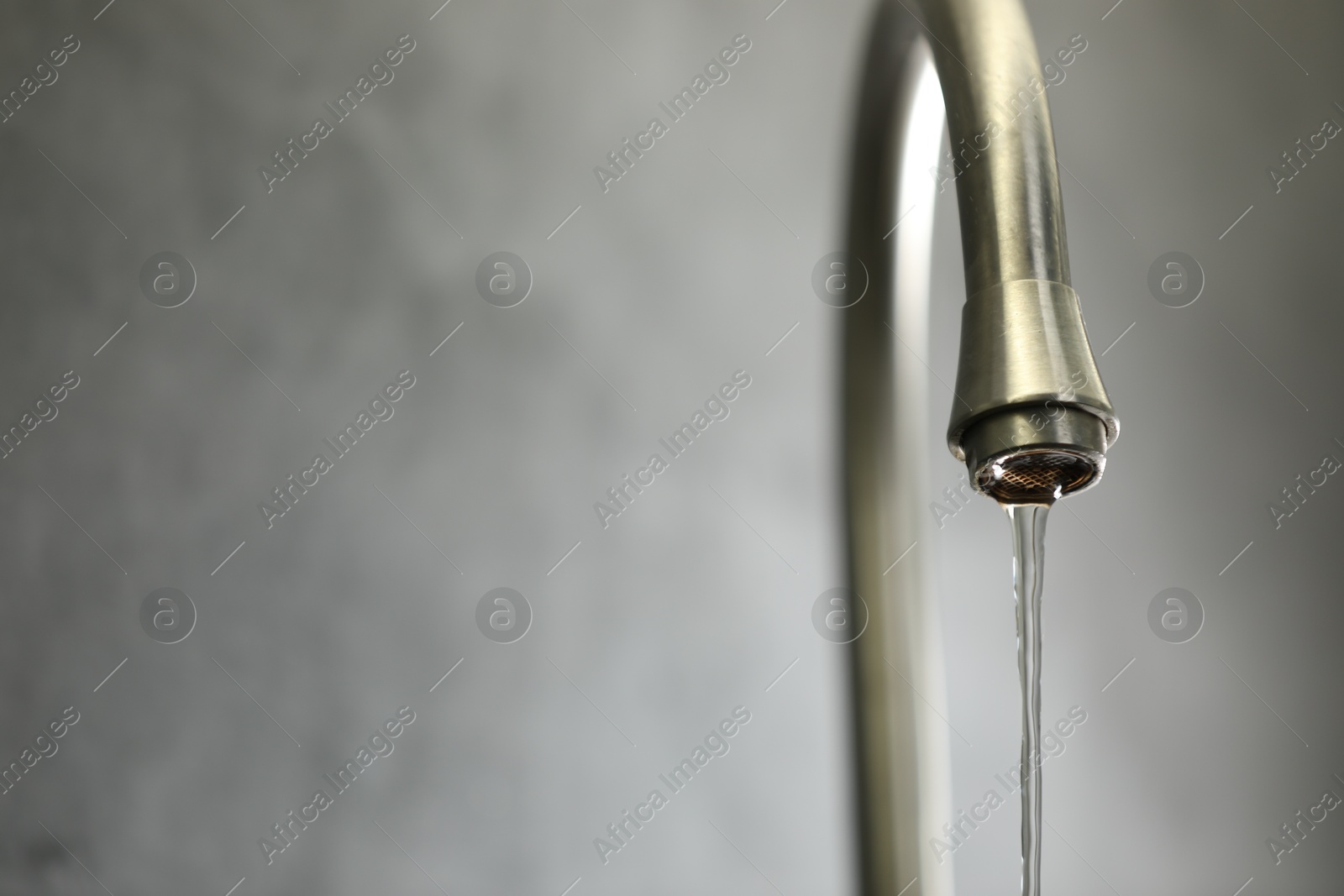 Photo of Save water concept. Stream of water flowing from tap against grey background, closeup. Space for text