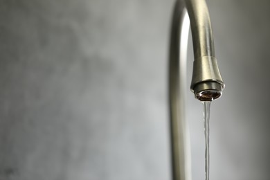 Photo of Save water concept. Stream of water flowing from tap against grey background, closeup. Space for text