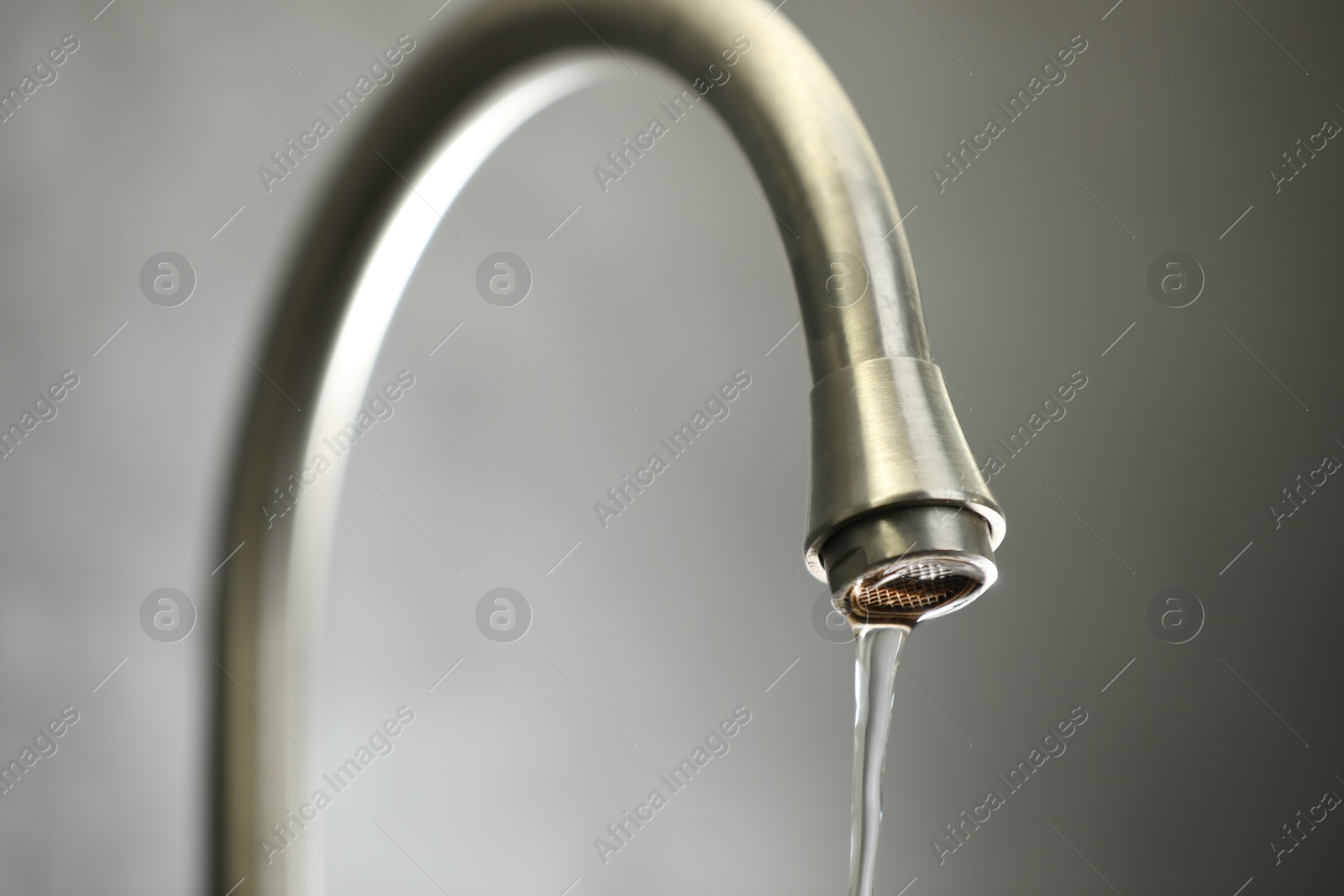 Photo of Save water concept. Stream of water flowing from tap against grey background, closeup