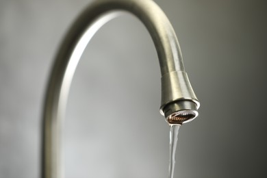 Photo of Save water concept. Stream of water flowing from tap against grey background, closeup
