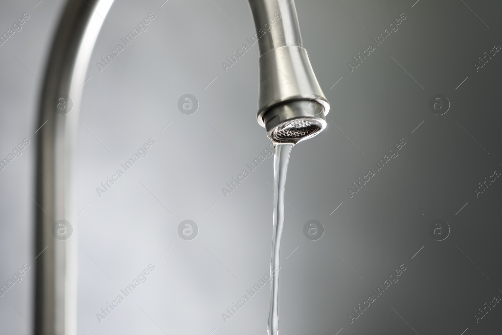 Photo of Save water concept. Stream of water flowing from tap against grey background, closeup