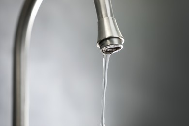 Photo of Save water concept. Stream of water flowing from tap against grey background, closeup