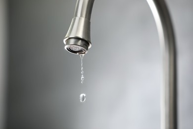 Photo of Water saving concept. Water dripping from tap against grey background, closeup. Space for text