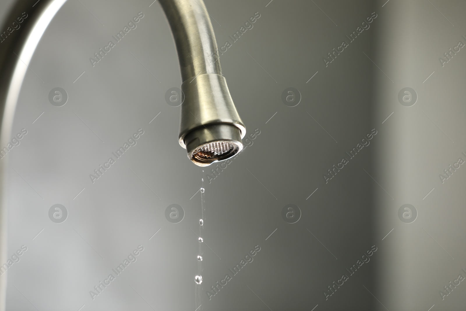 Photo of Water saving concept. Water dripping from tap against grey background, closeup. Space for text