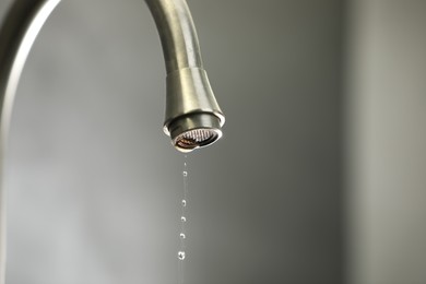 Photo of Water saving concept. Water dripping from tap against grey background, closeup. Space for text