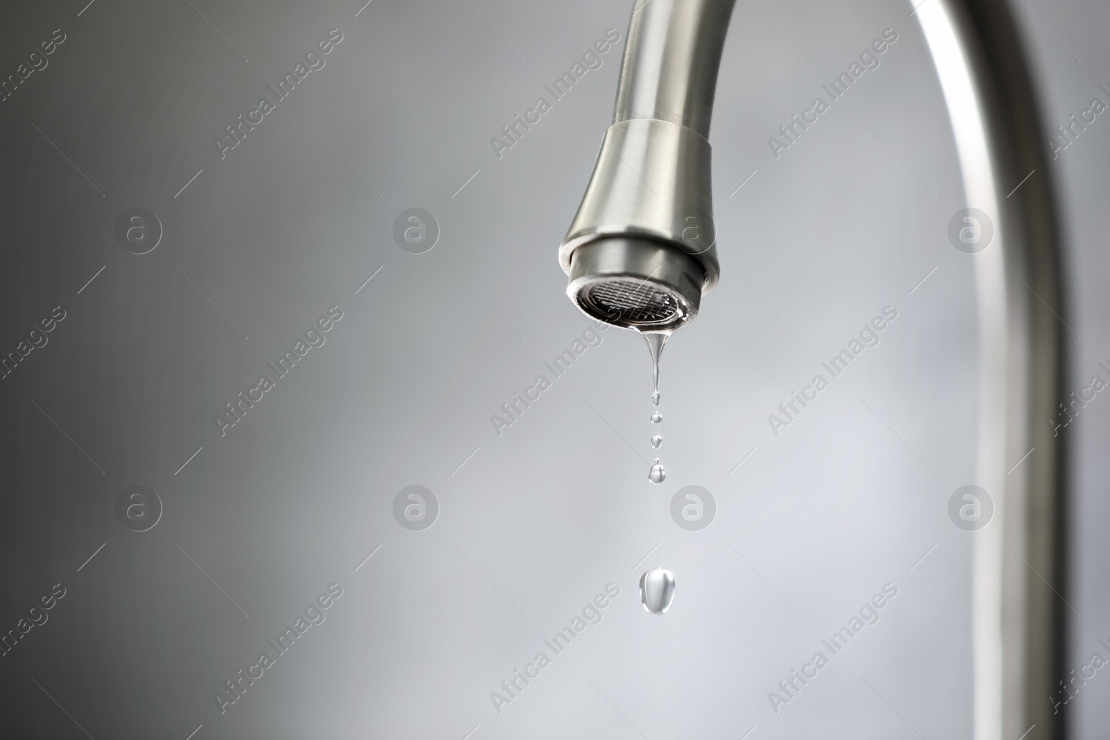 Photo of Water saving concept. Water dripping from tap against grey background, closeup. Space for text