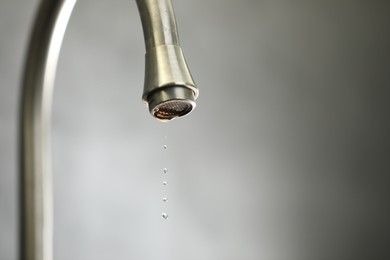 Photo of Water saving concept. Water dripping from tap against grey background, closeup. Space for text