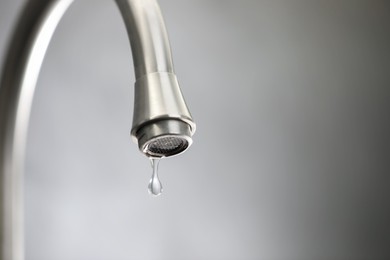 Photo of Water saving concept. Water dripping from tap against grey background, closeup. Space for text
