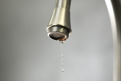 Photo of Save water concept. Water dripping from tap against grey background, closeup