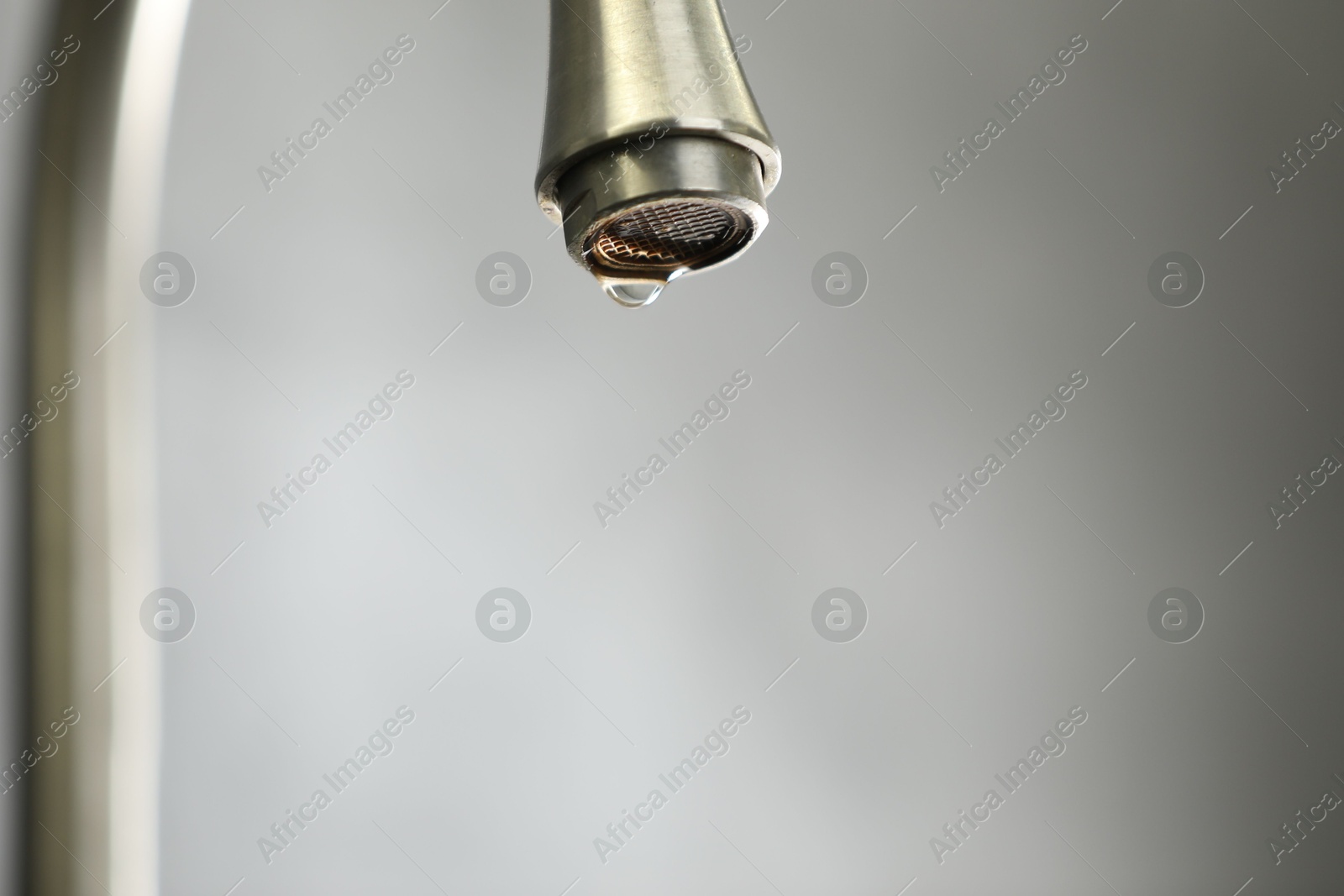 Photo of Water saving concept. Water dripping from tap against grey background, closeup. Space for text