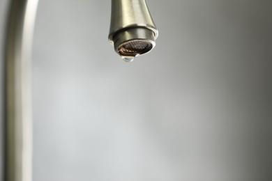 Photo of Water saving concept. Water dripping from tap against grey background, closeup. Space for text