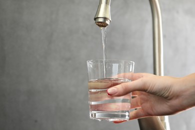 Photo of Water saving concept. Woman filling glass with tap water indoors, closeup