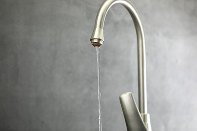Photo of Save water concept. Stream of water flowing from tap against grey background, closeup