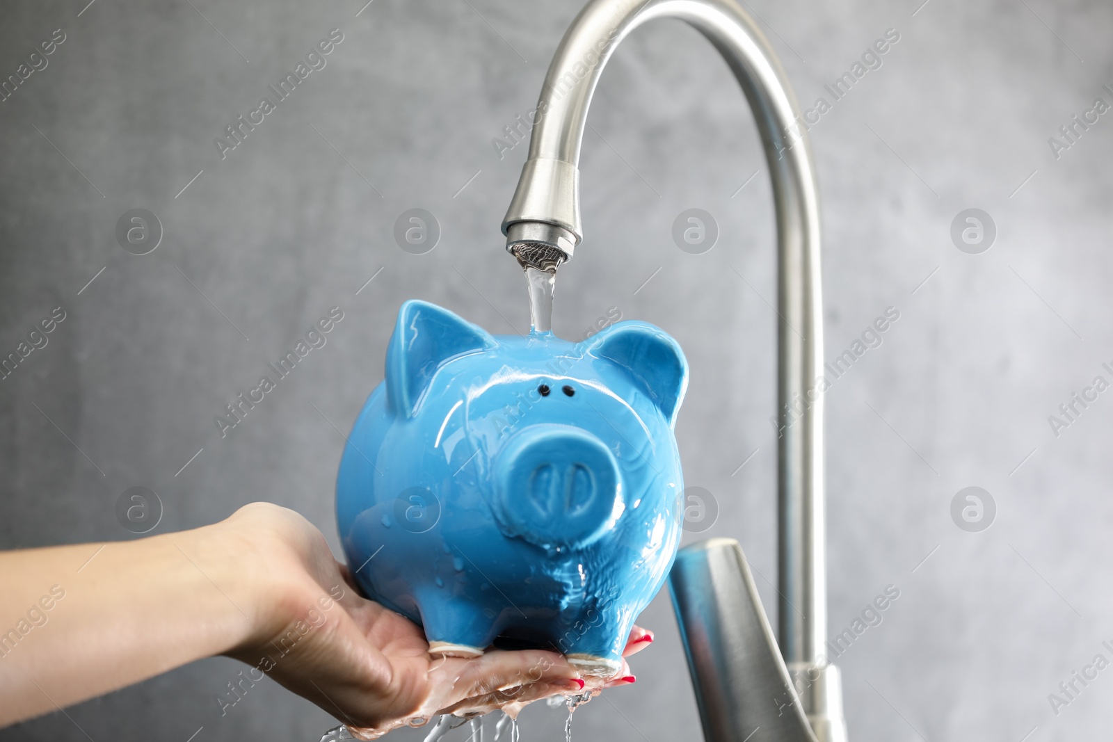 Photo of Water saving concept. Woman holding piggy bank under tap indoors, closeup