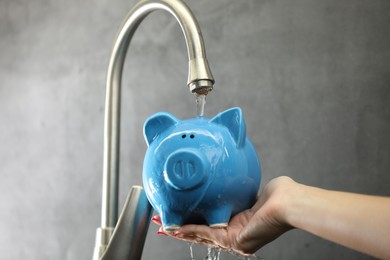 Photo of Water saving concept. Woman holding piggy bank under tap indoors, closeup