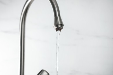 Photo of Save water concept. Stream of water flowing from tap against light background, closeup. Space for text