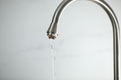 Photo of Save water concept. Stream of water flowing from tap against light background, closeup