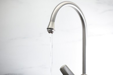Photo of Save water concept. Stream of water flowing from tap against light background, closeup
