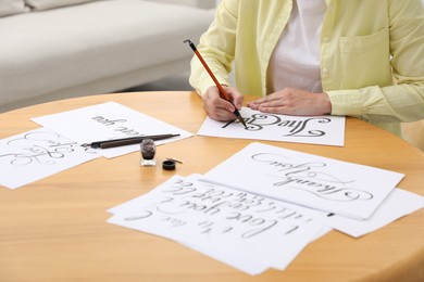 Photo of Calligraphy. Woman with brush writing words The End on sheet of paper at wooden table indoors, closeup