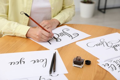 Photo of Calligraphy. Woman with brush writing words The End on sheet of paper at wooden table indoors, closeup