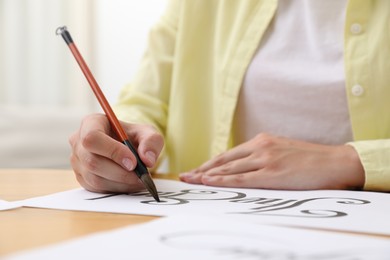 Photo of Calligraphy. Woman with brush writing words The End on sheet of paper at wooden table indoors, closeup