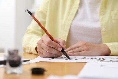 Photo of Calligraphy. Woman with brush writing words The End on sheet of paper at wooden table indoors, closeup