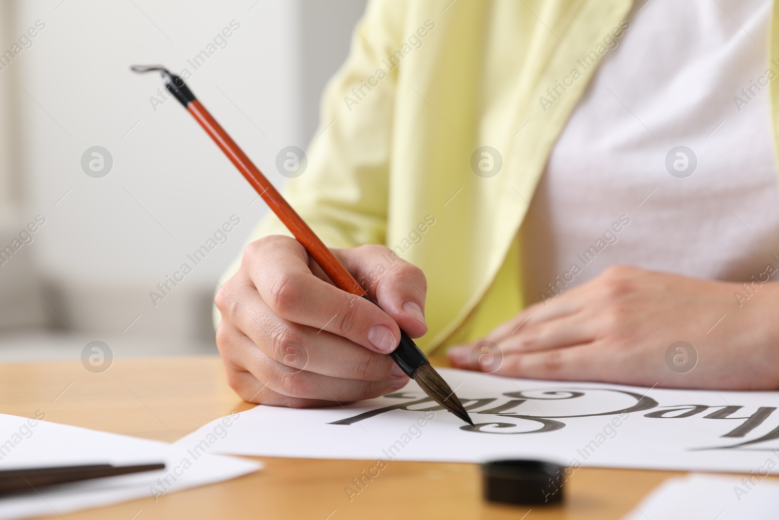 Calligraphy. Woman with brush writing words The End on sheet of paper at table indoors, closeup Photo of Calligraphy. Woman with brush writing words The End on sheet of paper at table indoors, closeup