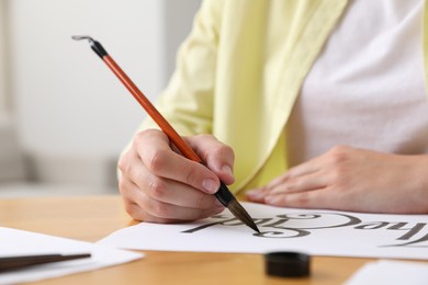 Photo of Calligraphy. Woman with brush writing words The End on sheet of paper at table indoors, closeup