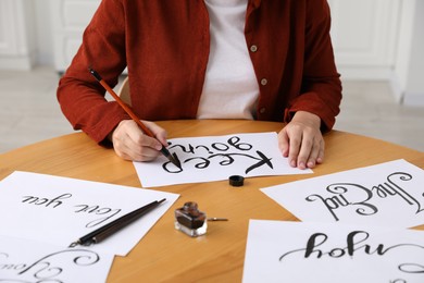 Photo of Calligraphy. Woman with brush writing phrase Keep Going on sheet of paper at wooden table indoors, closeup