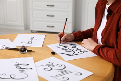 Photo of Calligraphy. Woman with brush writing phrase Keep Going on sheet of paper at wooden table indoors, closeup