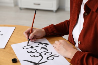 Photo of Calligraphy. Woman with brush writing phrase Keep Going on sheet of paper at wooden table indoors, closeup
