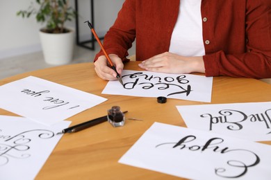 Photo of Calligraphy. Woman with brush writing phrase Keep Going on sheet of paper at wooden table indoors, closeup