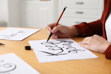 Photo of Calligraphy. Woman with brush writing phrase Keep Going on sheet of paper at wooden table indoors, closeup