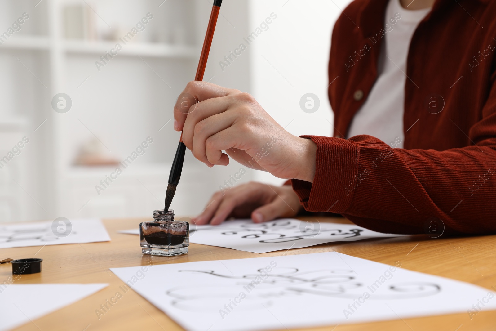 Calligraphy. Woman dipping brush into inkwell at wooden table indoors, closeup Photo of Calligraphy. Woman dipping brush into inkwell at wooden table indoors, closeup