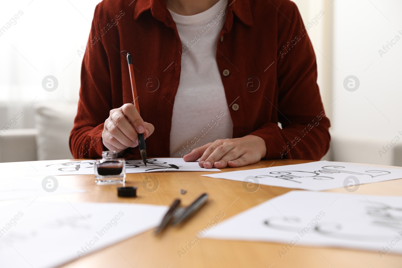 Photo of Calligraphy. Woman with brush writing phrase Keep Going on sheet of paper at wooden table indoors, closeup