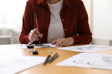 Photo of Calligraphy. Woman with brush writing phrase Keep Going on sheet of paper at wooden table indoors, closeup