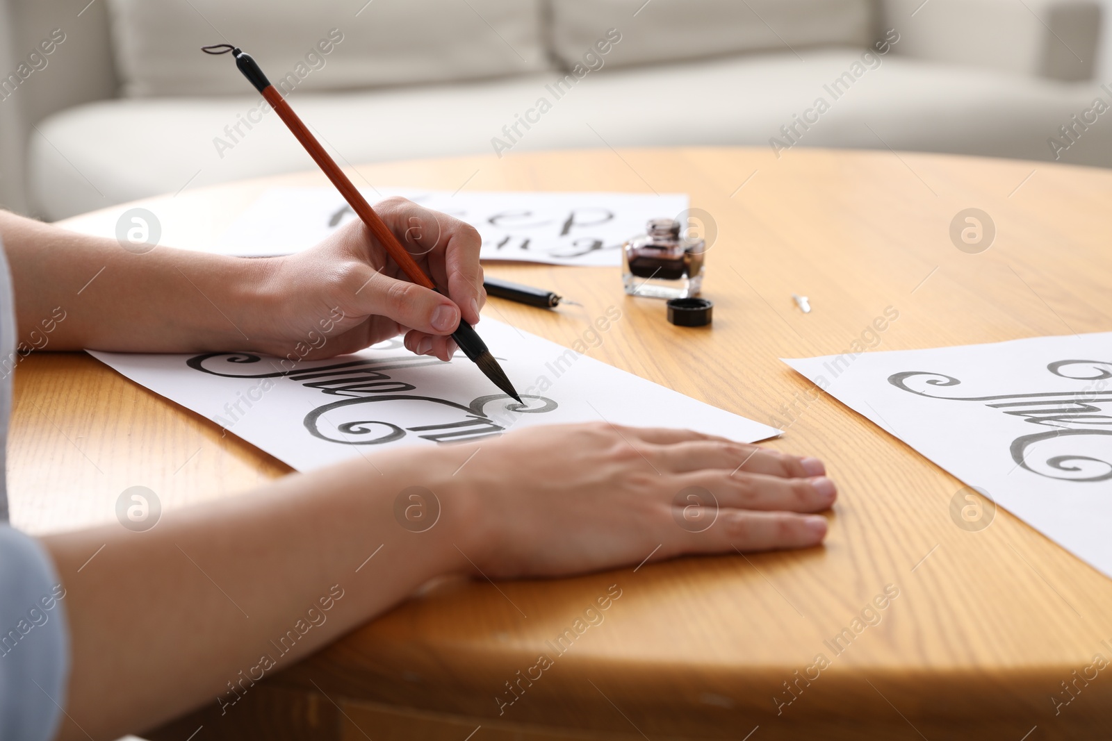 Photo of Calligraphy. Woman with brush writing words The End on sheet of paper at wooden table indoors, closeup