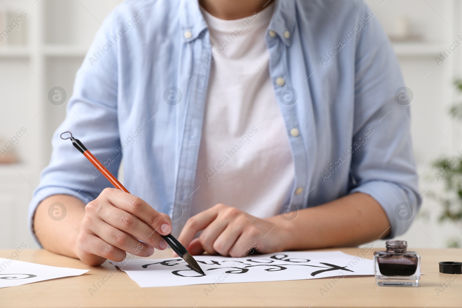Photo of Calligraphy. Woman with brush writing phrase Keep Going on sheet of paper at wooden table indoors, closeup