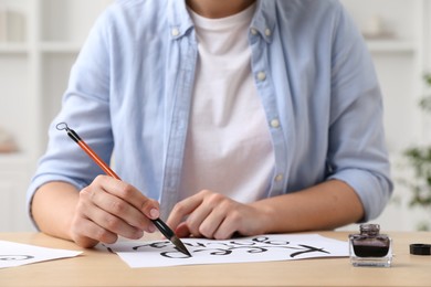 Photo of Calligraphy. Woman with brush writing phrase Keep Going on sheet of paper at wooden table indoors, closeup
